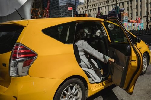 Open rear passenger door of a yellow car with a person getting in.