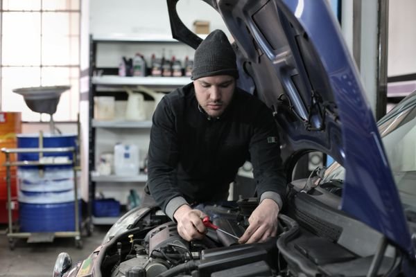 Mechanic working on a car engine with the hood open in a workshop.