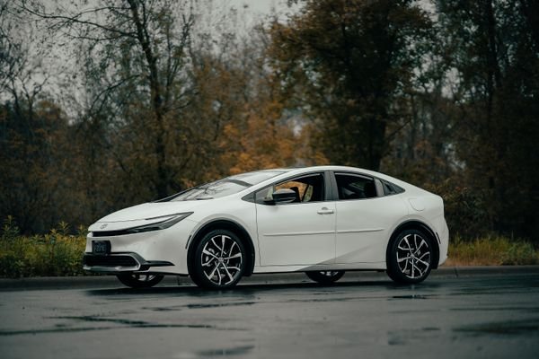White Toyota Prius hybrid car parked on a wet road.