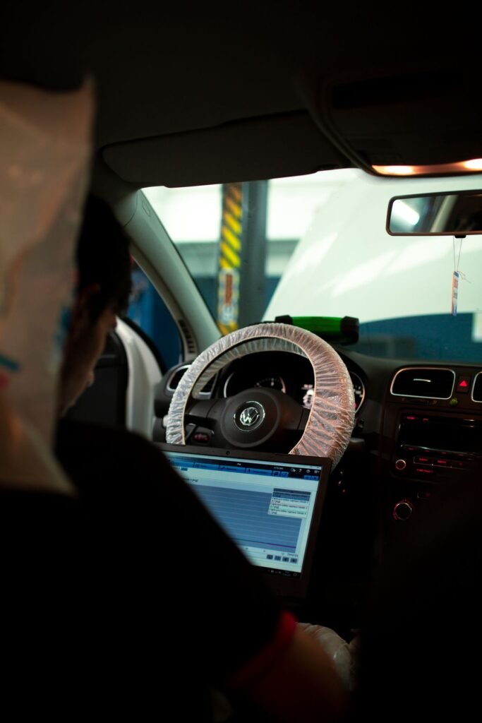 Mechanic sitting inside a car using a laptop for diagnostics