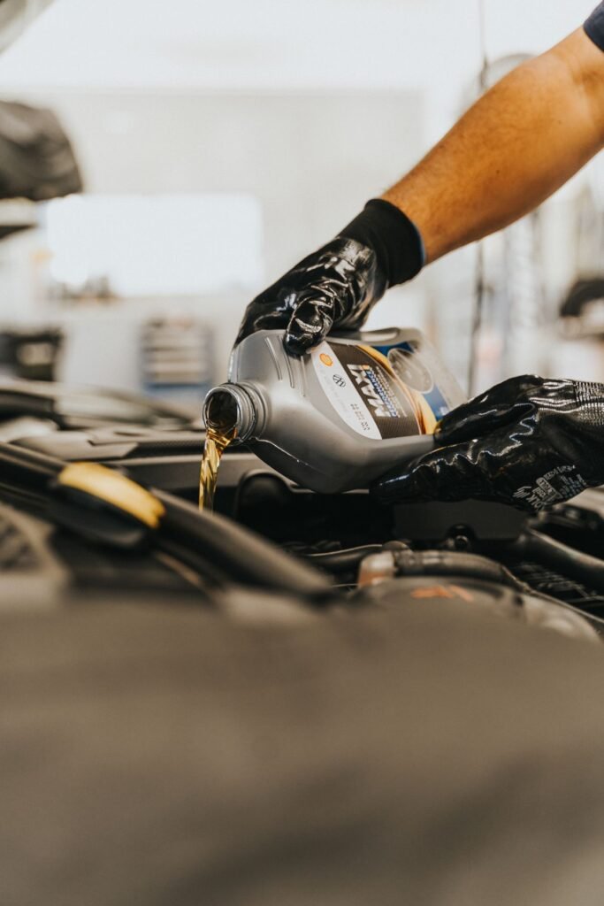 Close up of a mechanic with gloved hands pouring engine oil into a car engine
