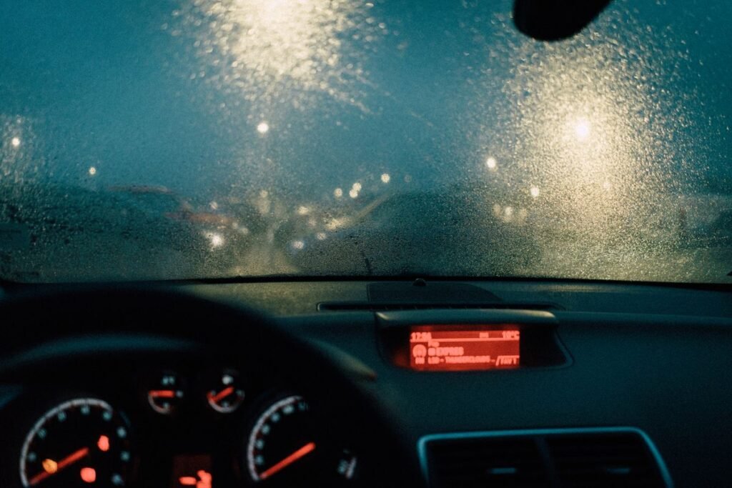 View from inside a car with raindrops on the windshield and blurred lights at night