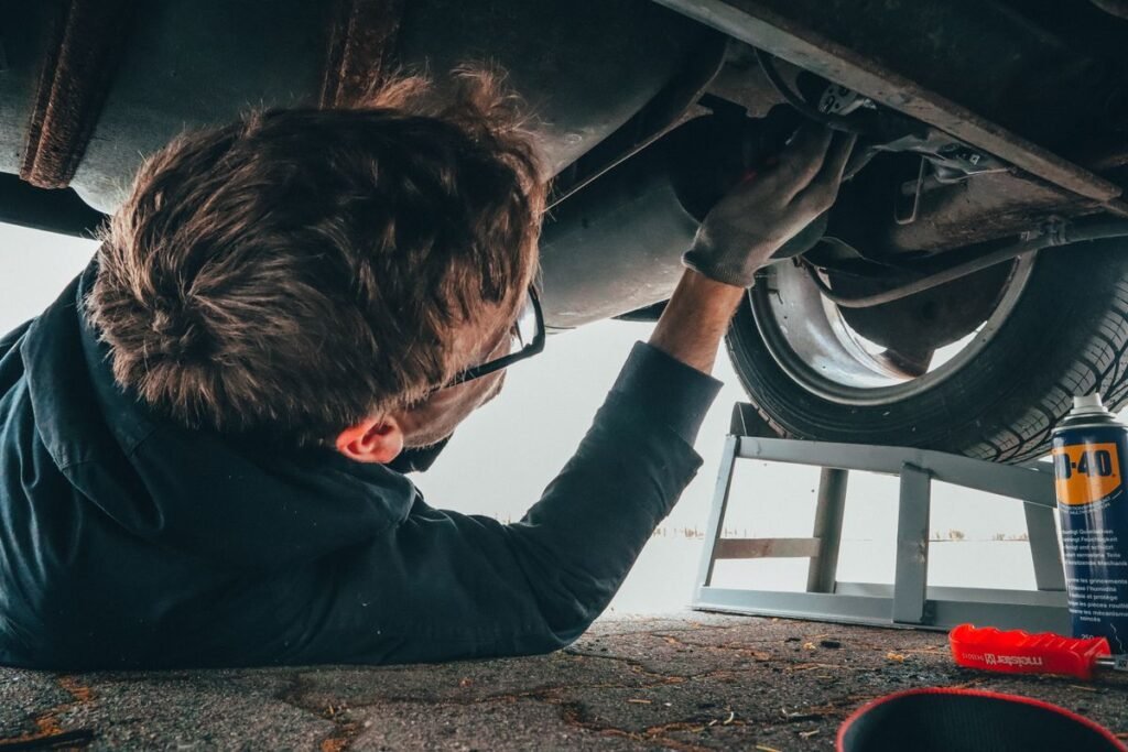 Mechanic repairing a car undercarriage outdoors with tools, gearbox area work
