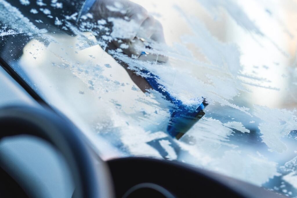 Hand scraping ice off a car window on a cold morning