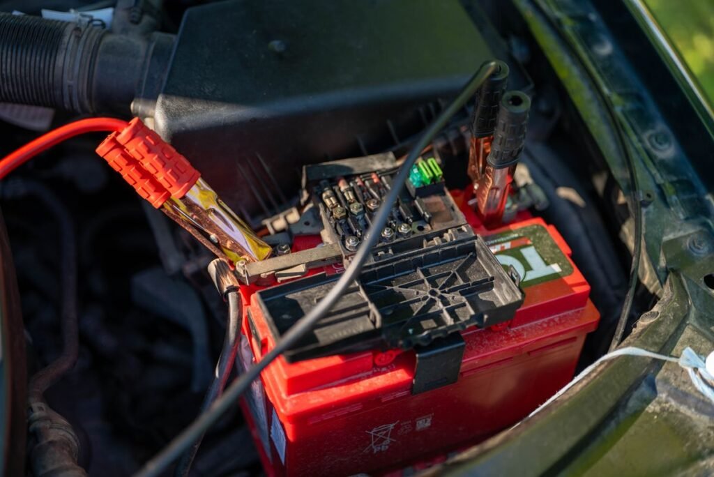 Close up of a car battery with red jumper cables connected in the engine bay, outdoors