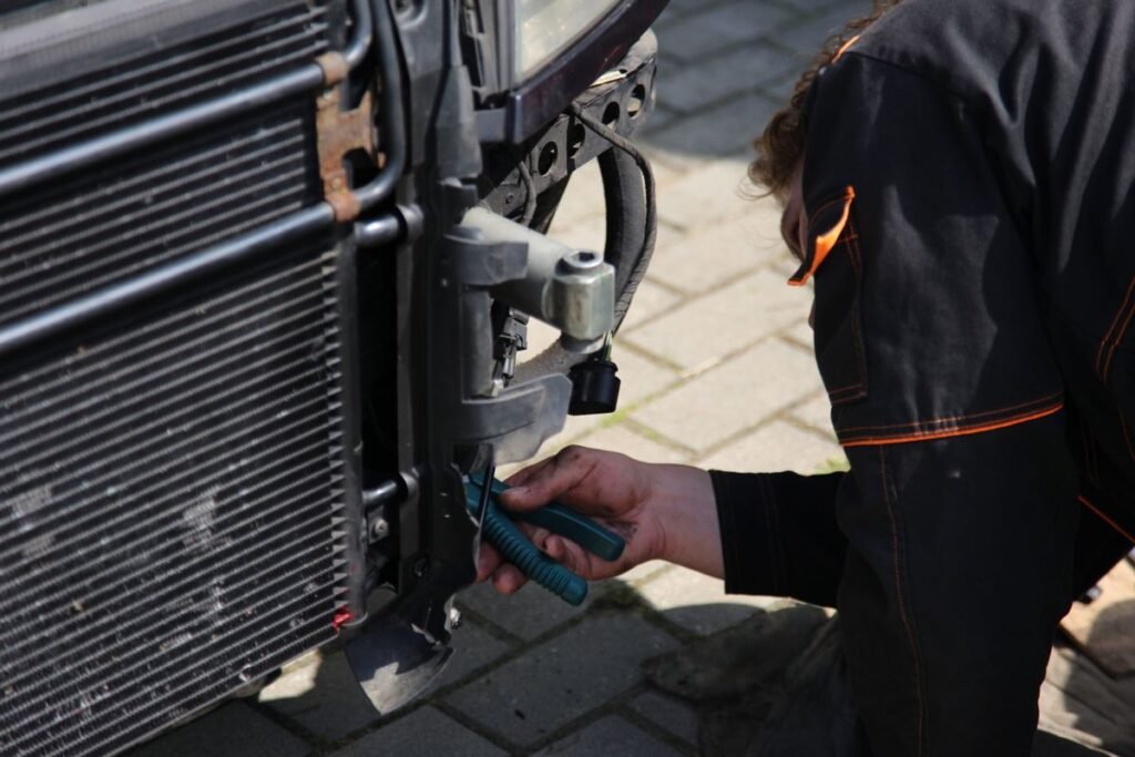 Mechanic repairing a car outdoors with tools around the radiator area