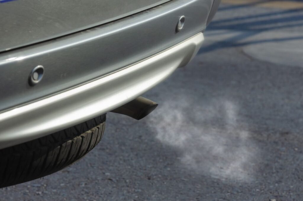 Close up of a silver car exhaust pipe emitting smoke on the road