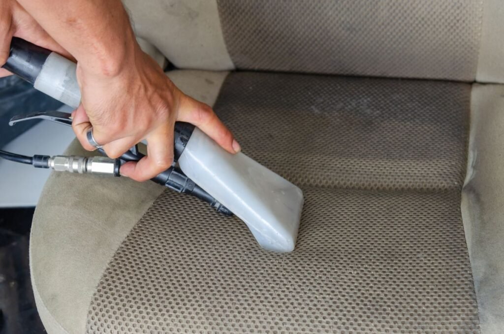 Hands using a vacuum nozzle to deep clean a fabric car seat