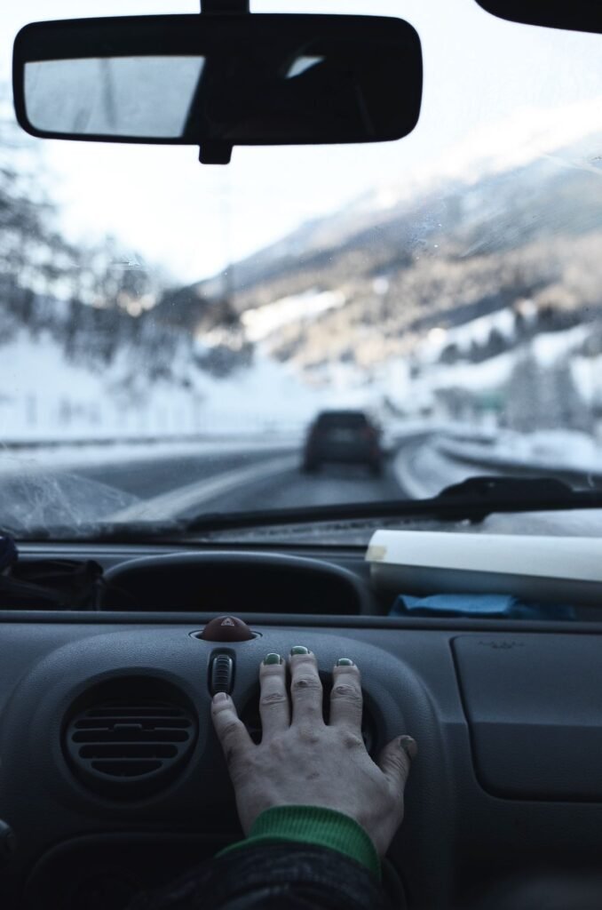 Hand resting on a car air vent while driving through snowy mountains