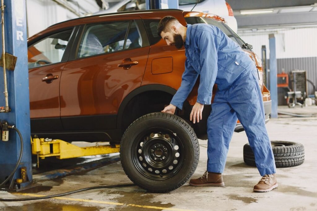 Mechanic in blue coveralls replacing a tire on a red SUV in a repair shop garage