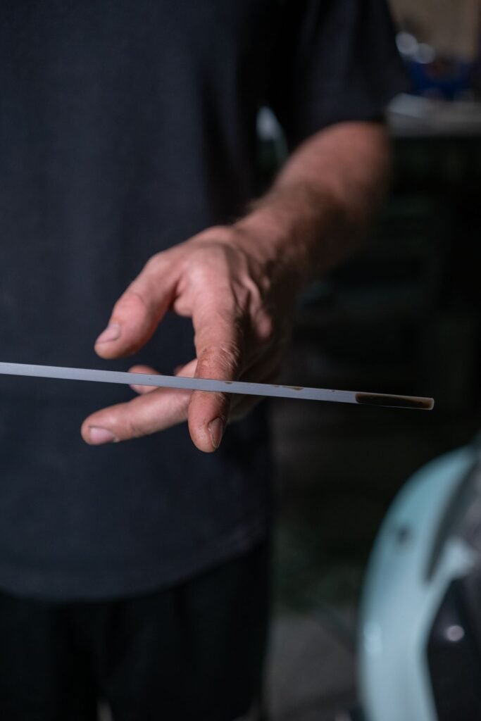 Close up of a hand holding an engine oil dipstick to check the oil level in a garage