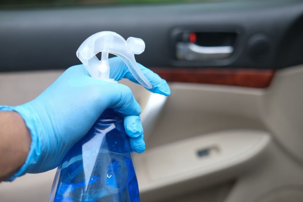 Close up of a gloved hand holding a blue spray bottle while cleaning and freshening a car interior