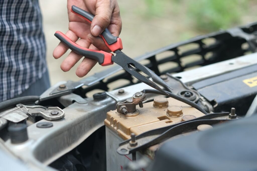 Person using pliers to check a car battery in an outdoor setting