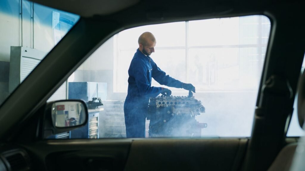 Mechanic in blue overalls working on an engine with steam rising in a garage