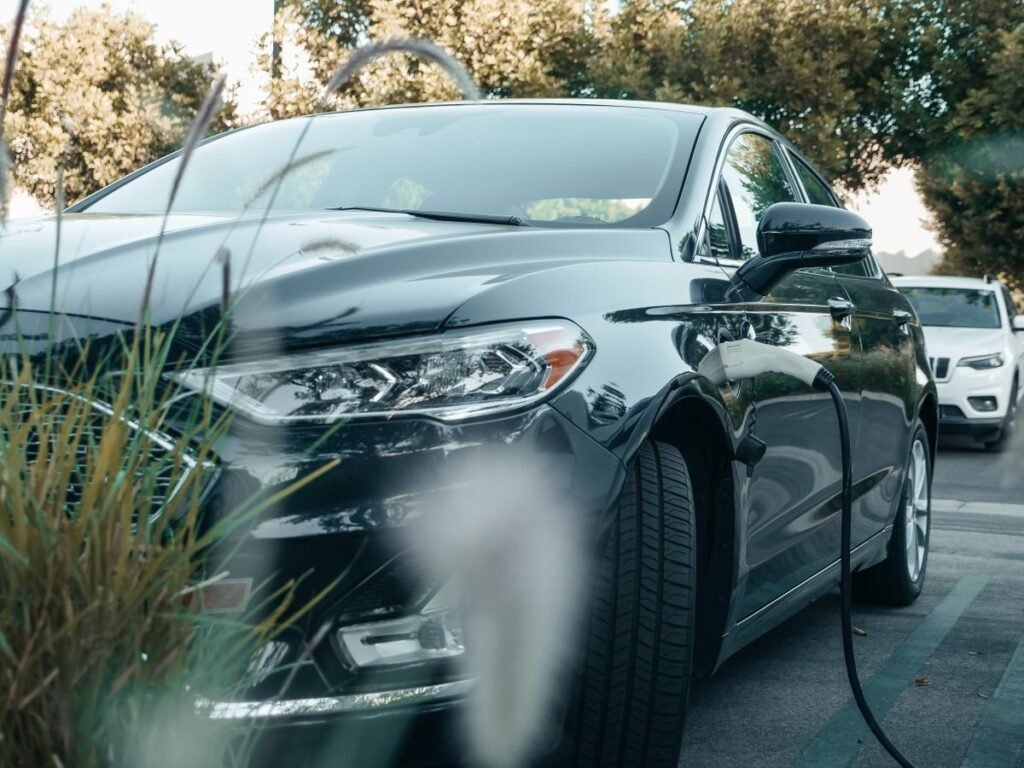 Black plug in hybrid car charging at an outdoor station surrounded by greenery