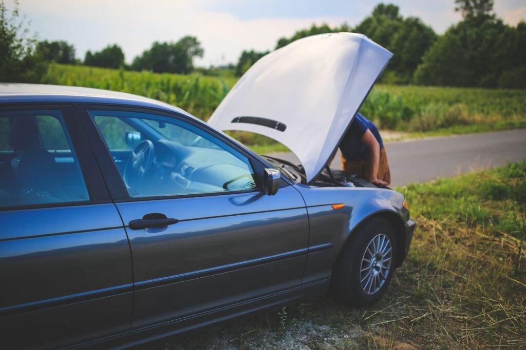 Man checking the engine of a broken car with the hood open at the roadside